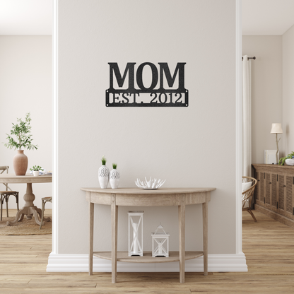 scripted MOM plaque with personalized  date of motherhood, powder coated black finish metal wall decor, hanging over a small wooden table on a creamy white wall | Home Accent Studio